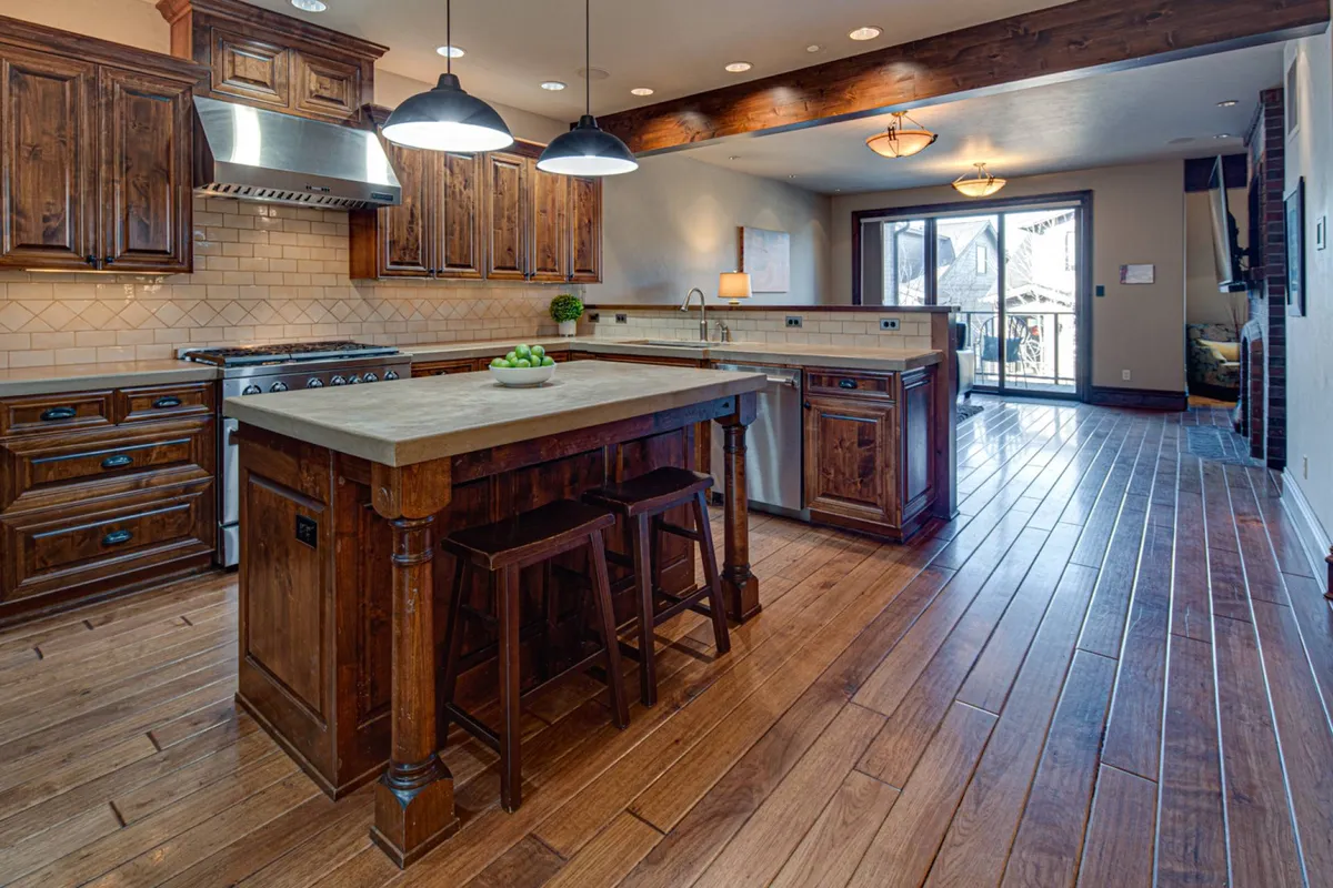 This image captures a spacious kitchen featuring a central island with stools, sleek high-end appliances, and inviting wooden cabinetry. The open layout and visible sliding door suggest a seamless flow between indoor and outdoor spaces, highlighting both the breakfast bar and cooking areas.