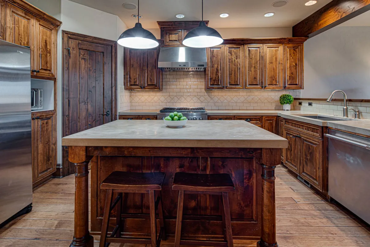 The gourmet kitchen shines with a spacious island, pendant lights, wooden cabinets, stainless steel appliances, and a countertop adorned with a fruit bowl. The space feels warm, welcoming, and well-equipped for hosting festive dinners or casual mornings over coffee.