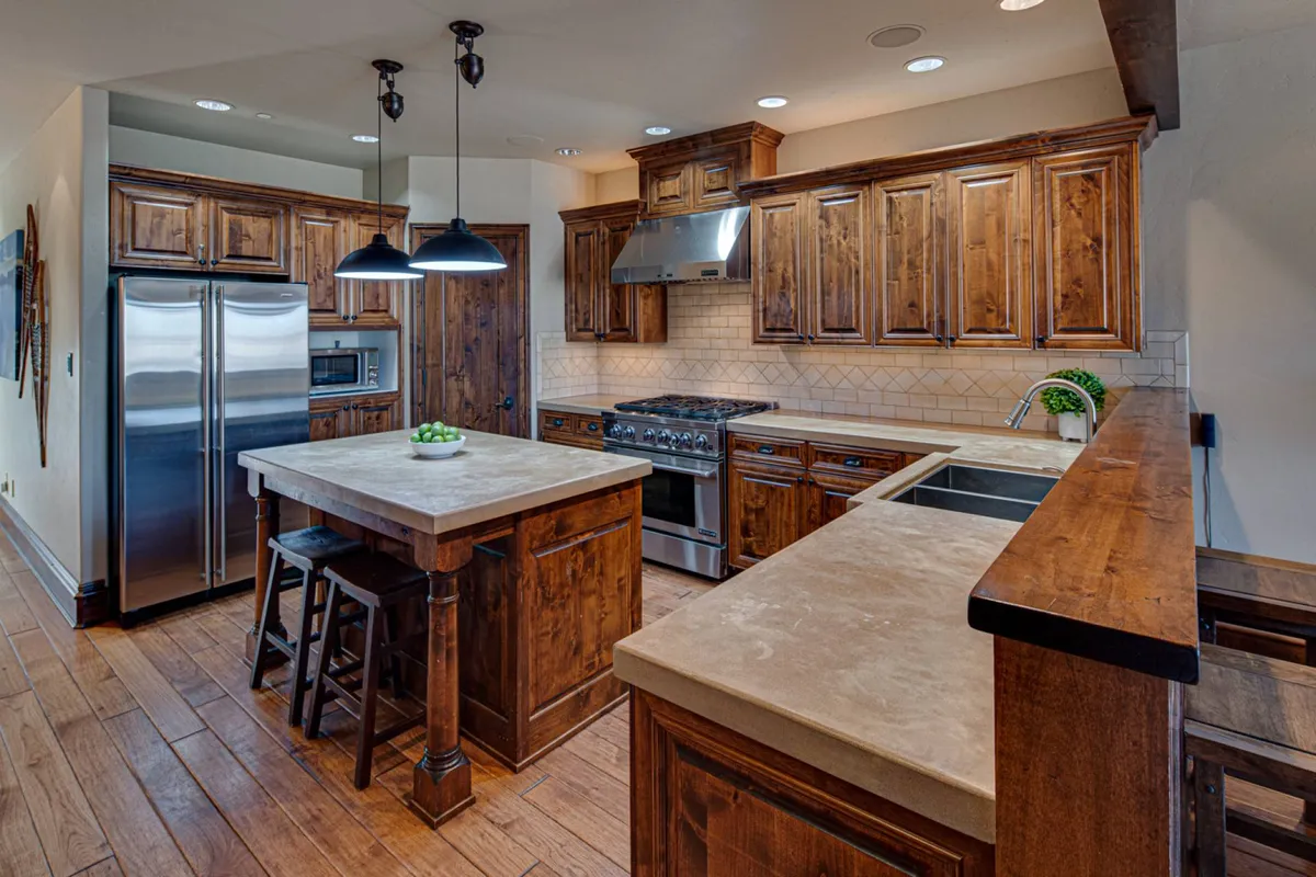 A modern kitchen scene with a large island, stylish wooden cabinetry, stainless steel appliances, and pendant lighting. The setting feels lively and ready for cooking or entertaining, with ample space for family and guests to gather.