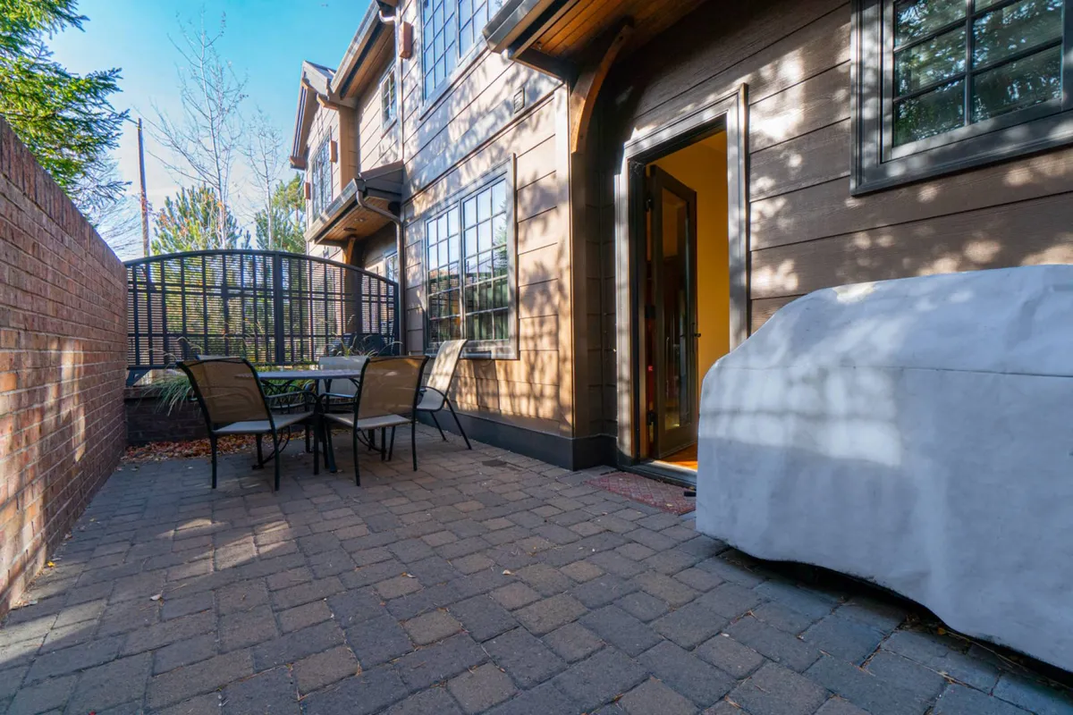A welcoming exterior patio area featuring a table and chairs set for outdoor dining, with a covered vehicle parked nearby and the entrance door visible. The patio exudes a casual, inviting atmosphere and is ideally suited for pet owners seeking a space for supervised outdoor relaxation with their dogs.