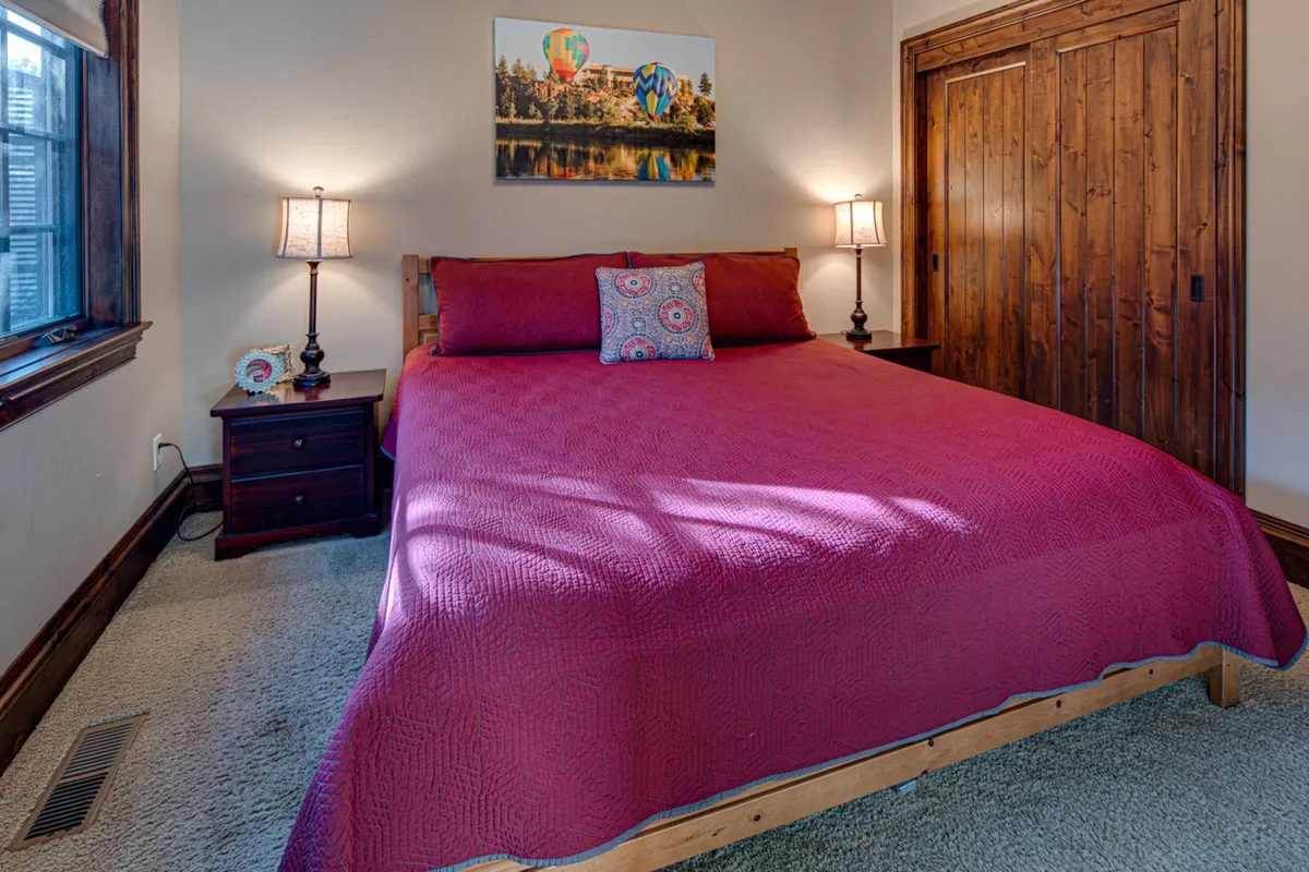 A welcoming bedroom with a neatly made bed, bedside lamps, wall art, and a window-side reading nook. The space is suffused with soft daylight, creating an inviting spot for restful sleep or quiet moments.