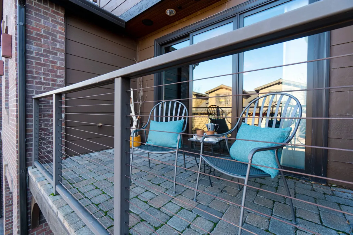 A private balcony features two cushioned chairs and a small table, surrounded by a sleek railing. The setting is perfect for sipping morning coffee, soaking in sunrise views, or enjoying a quiet evening looking out over the cityscape.