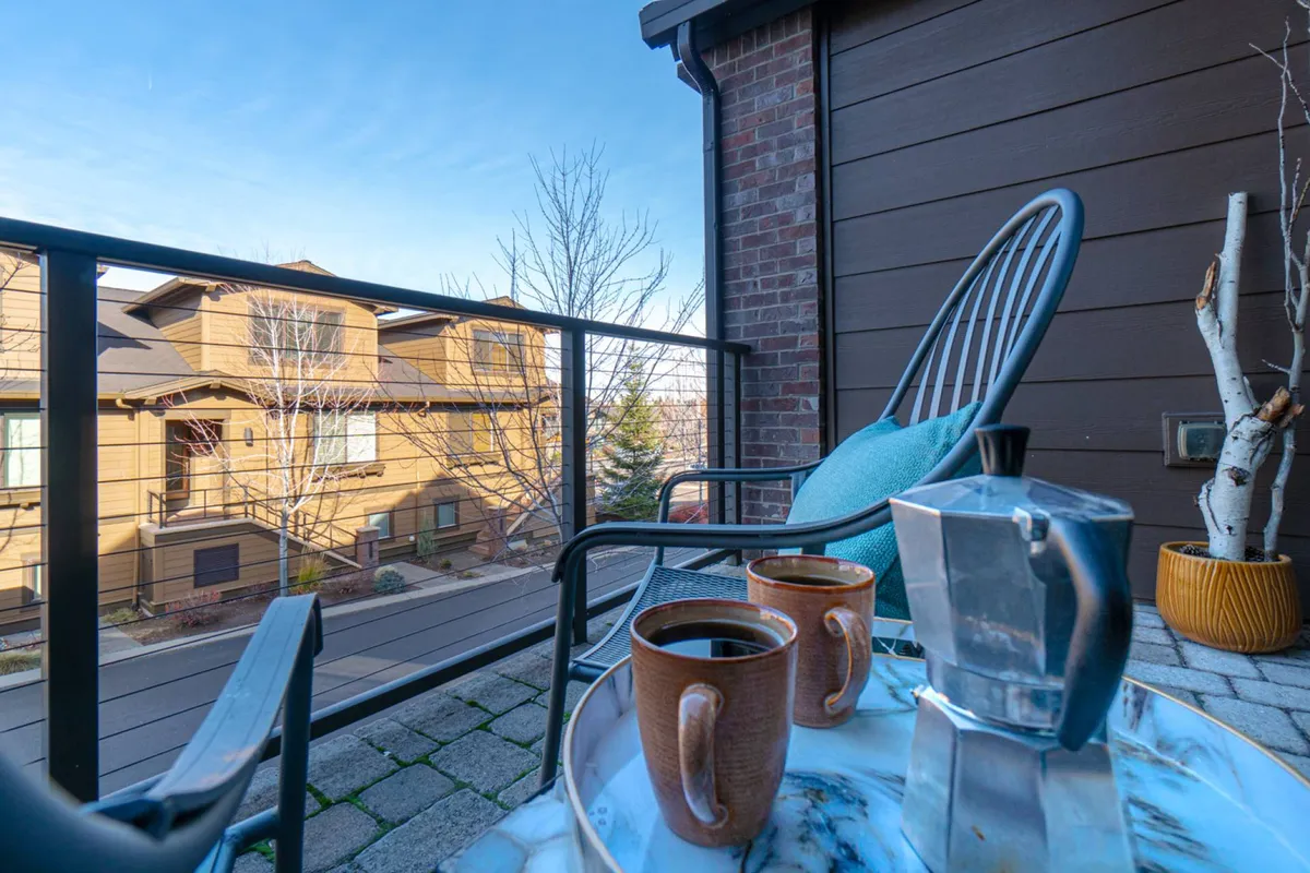 A serene patio scene with cozy chairs, coffee cups, and a marble tray overlooking the neighborhood. The space suggests tranquil, private outdoor enjoyment, perfect for relaxing with a pet close by.