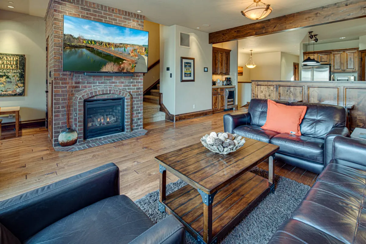 The image showcases a warm and inviting living room with a modern fireplace, plush couch, sleek coffee table, and a large television. Sunlight filters in, accentuating the cozy ambiance and highlighting spaces perfect for relaxing, socializing, or unwinding after a day of adventure.